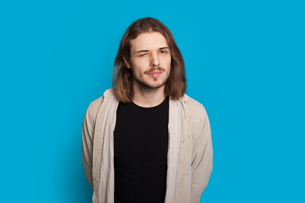 Bearded caucasian man with long hair is blinking while posing on a blue background