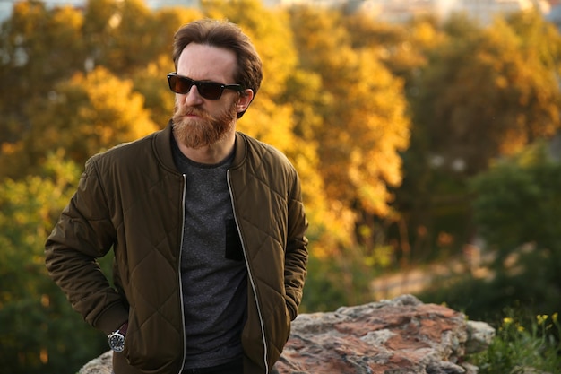 Bearded Caucasian man with sunglasses posing in front of a blurry background with soft natural light
