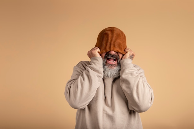 Bearded Caucasian man with woolen cap covering his eyes with a big smile of excitement and surprise.