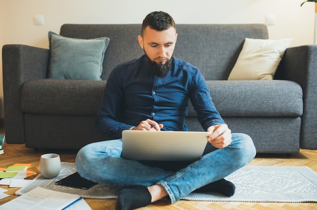 Bearded caucasian man working with his notebook on floor in the living room