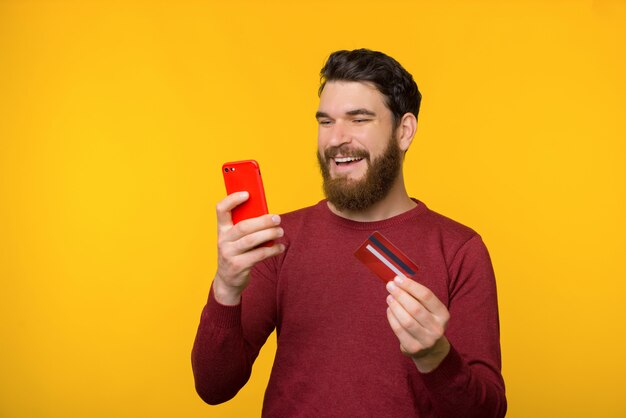 Bearded cheerful man is shopping online from smartphone.