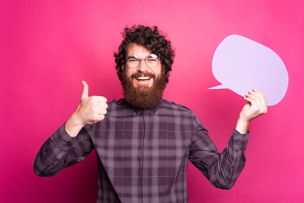 Bearded cheerful man is showing a thumb up and a speech bubble