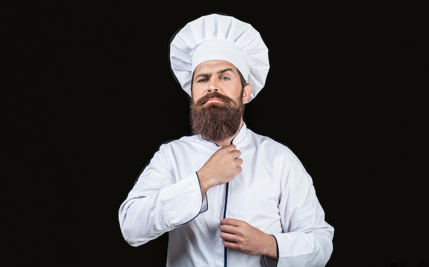 Bearded chef cooks or baker Bearded male chefs isolated on black Cook hat Confident bearded male chef in white uniform Serious cook in white uniform chef hat Portrait of a serious chef cook