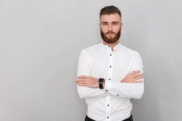 bearded confident man looking at front with arms crossed isolated over gray wall