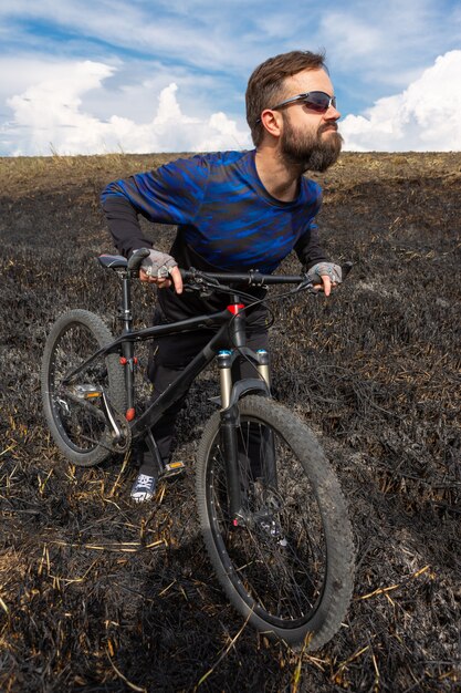 Bearded cyclist on a mountain bike on a burned field