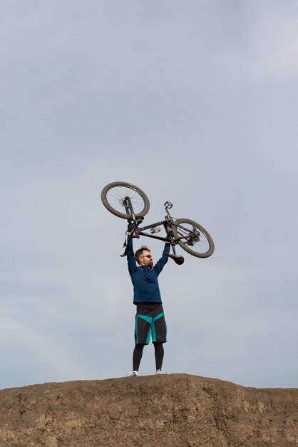 山のひげを生やしたサイクリストは、頭の上の腕に自転車を持っています