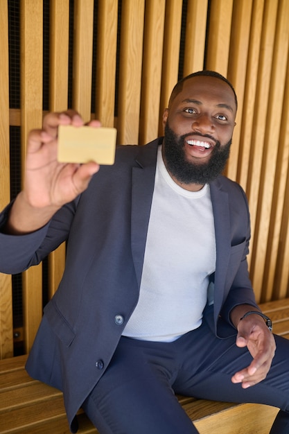 A bearded dark-skinned smiling man holding a credit card