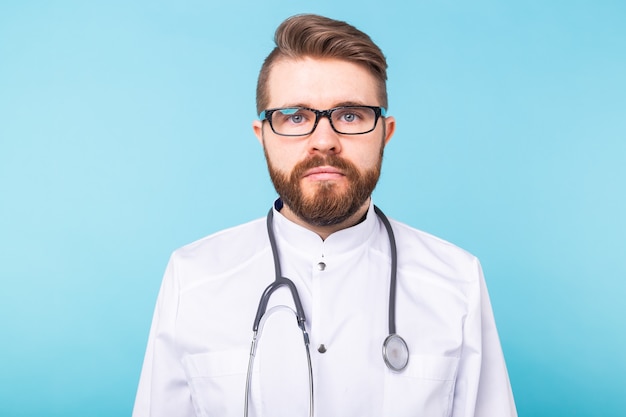Bearded doctor standing with stethoscope over blue wall. Medicine, healthcare and people