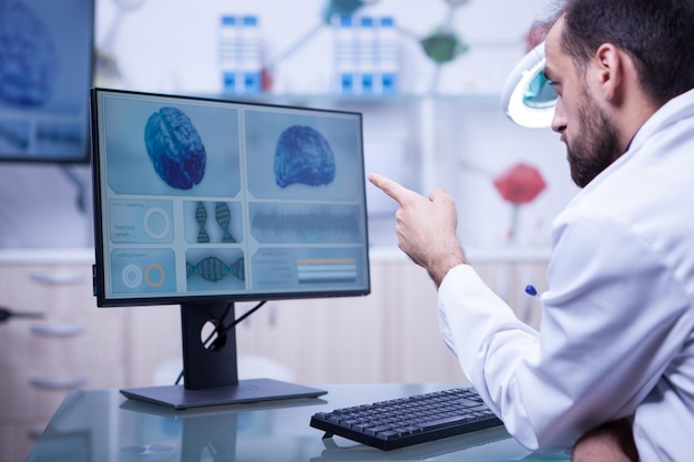 Bearded doctor in white coat pointing at a brain x-ray on the monitor. Doctor giving a diagnostic.