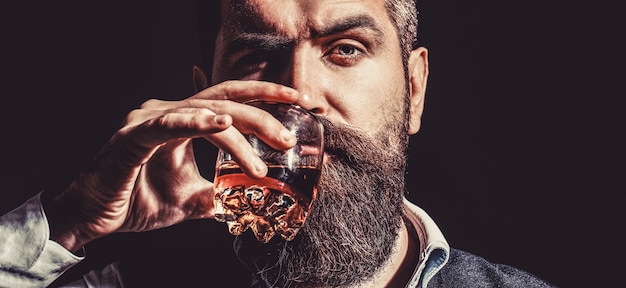 Bearded drink cognac. Sommelier tastes drink. Man holding a glass of whisky. Sipping whiskey. Portrait of man with thick beard. Macho drinking. Degustation, tasting