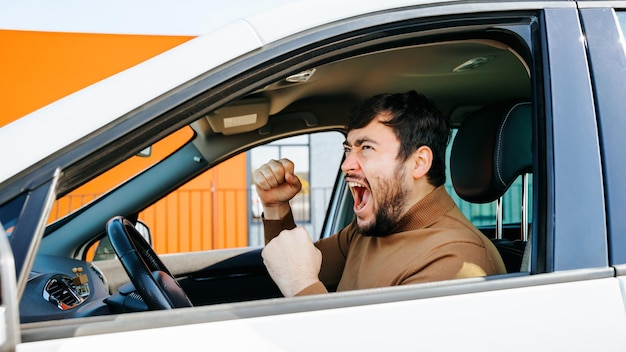 bearded driver is violent and screaming inside the vehicle behind the wheel nice caucasian man with open mouth is irritated side view