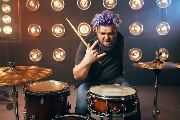 Bearded drummer with colorful hair, rock performer on the stage with lights