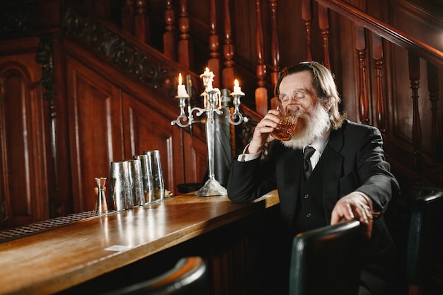 Photo bearded elderly businessman. man drinks a whiskey. senior in black suit.