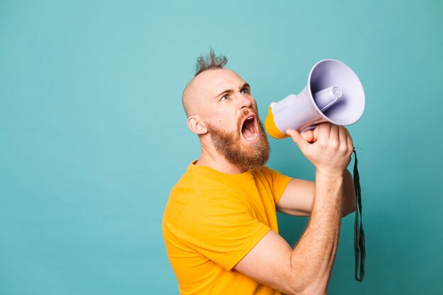 Bearded european man in yellow shirt isolated, crazy shouting in megaphone loudspeaker, attention!