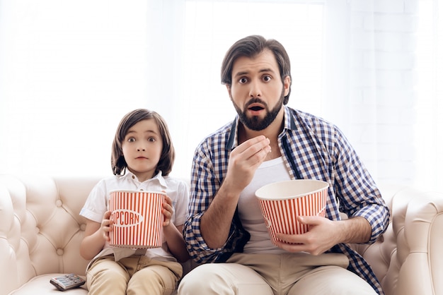 Bearded father with small son is watching thrilling film.