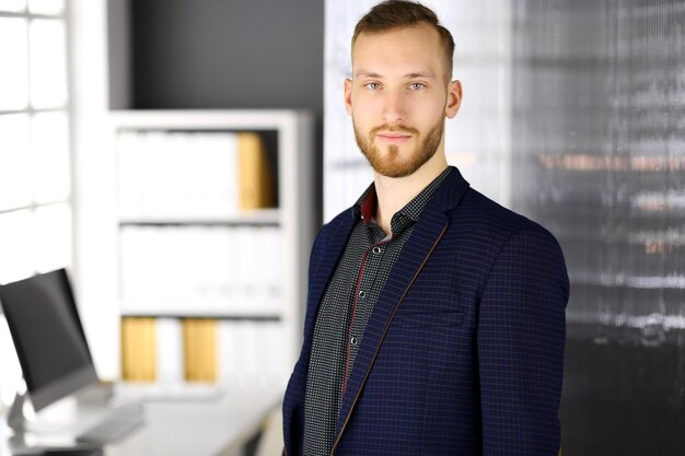 Bearded friendly adult businessman looking at camera. Business headshot or portrait in office.