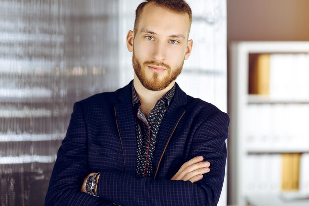 Bearded friendly adult businessman looking at camera. Business headshot or portrait in sunny office.