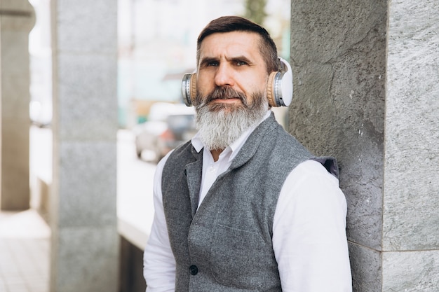 Bearded gray-haired senior man listening to music on the urban space