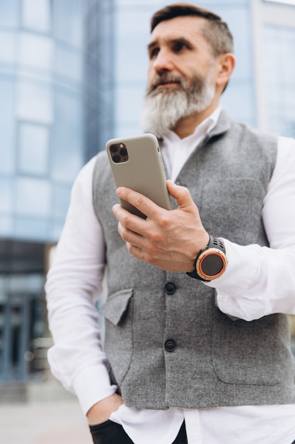 A bearded gray-haired senior man uses and talks on a smartphone