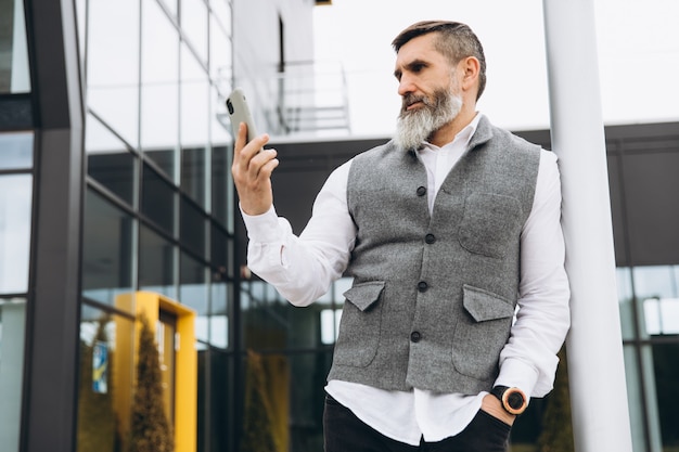 A bearded gray-haired senior man uses and talks on a smartphone