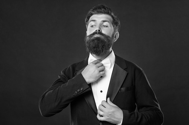 Bearded groom in tuxedo on black background suit