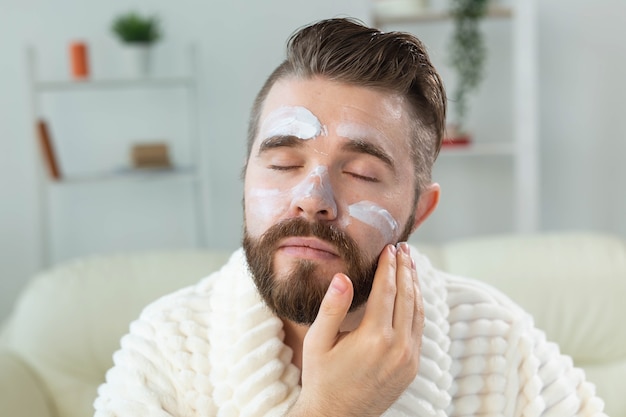 Bearded guy applying anti-wrinkle cream on his face. Skin care and spa for man concept.