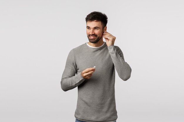 Bearded guy in grey sweater putting on wireless earphones