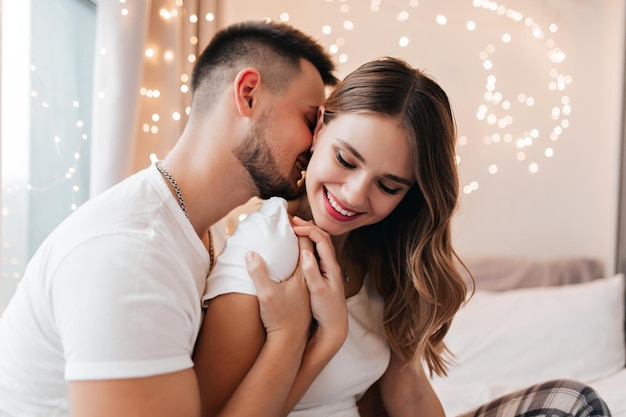 Tipo barbuto che bacia la sua ragazza nel collo. servizio fotografico romantico al coperto di una giovane coppia felice.