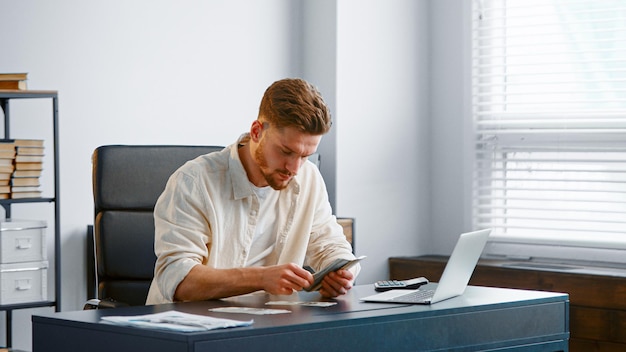 Bearded guy manager counts dollar banknotes and puts in stack on grey office table