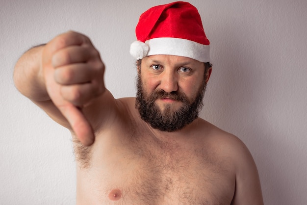 Бородатый полуобнаженный Санта-Клаус показывает жест большим пальцем вниз одной рукой