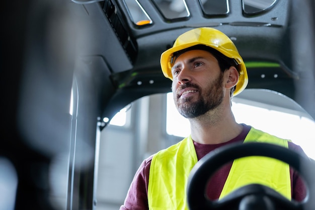 Bearded handsome man worker driver wearing hard hat work wear driving forklift looking away