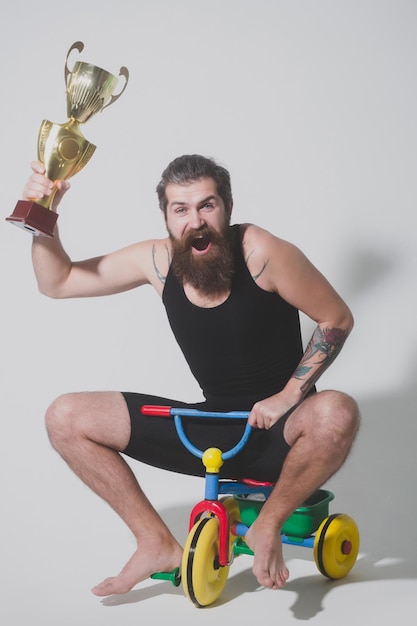 Bearded happy man holds gold champion cup on bicycle toy