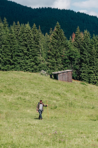 Bearded hiker man in dark clothes and with a backpack walks on\
a mountain meadow