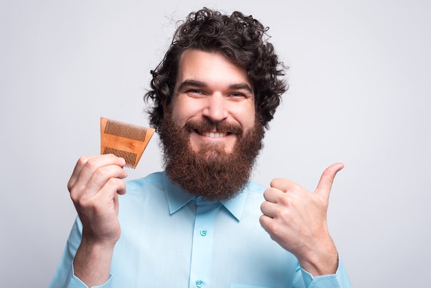 bearded hipster man holding hairbrush and showing thumb up.