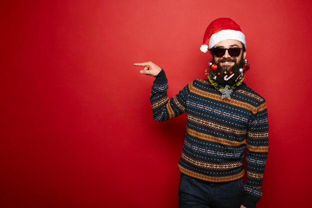 Bearded hipster man in santa hat gesturing to left