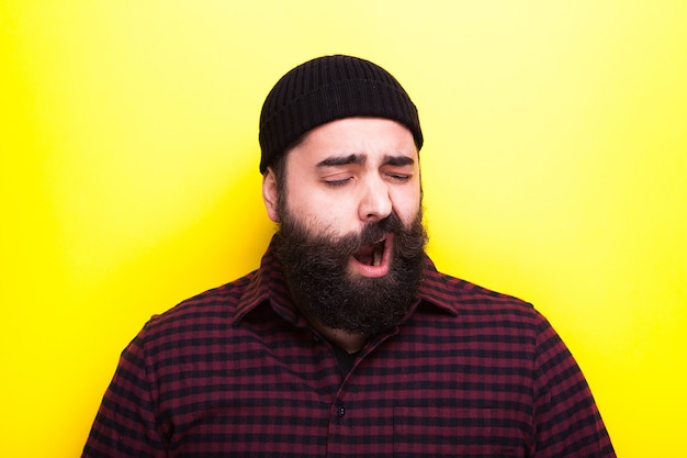 Bearded hipster man yawning on yellow background