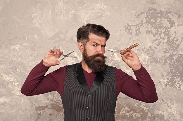 Foto barbuto hipster rasatura barbiere barbuto tenere strumenti per parrucchieri creare nuova acconciatura barbiere attrezzature retrò di lama tagliata e forbici uomo serio con barba brutale maestro barbiere