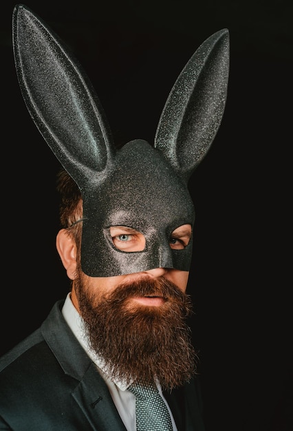 Bearded hipster in suit is ready for carnival Funny bearded man in carnival rabbit mask Handsome man in carnival mask ballroom rabbit with long ears sensual on a black background