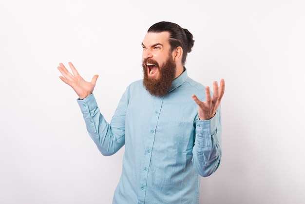 Foto hipster barbuto che indossa una camicia azzurra urla e tiene le braccia spalancate.