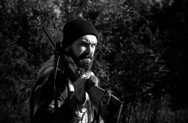 Bearded hunter man holding gun and walking in forest hunter with shotgun gun on hunt