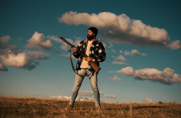 Photo bearded hunter man holding gun and walking in forest hunter with shotgun gun on hunt