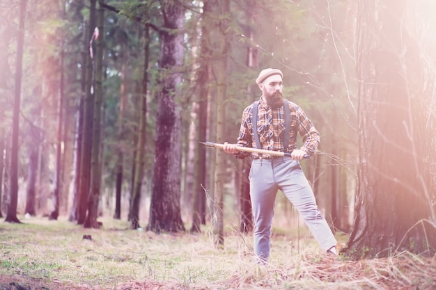 A bearded lumberjack with a large ax examines the tree before felling