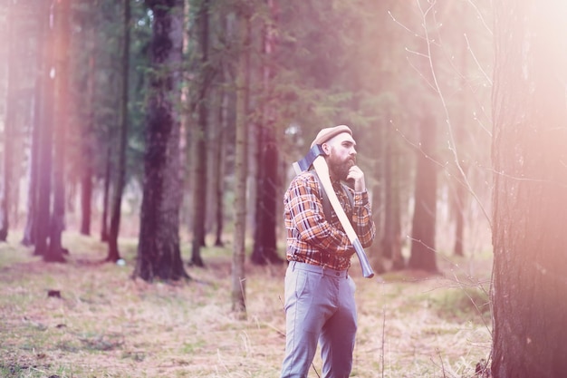 A bearded lumberjack with a large ax examines the tree before felling