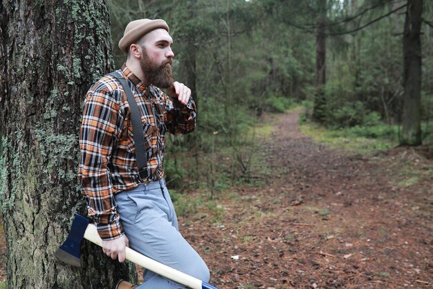 A bearded lumberjack with a large ax examines the tree before felling