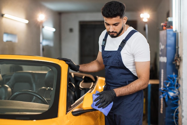 Bearded male car service worker in black rubber glove and overalls holding the microfiber cloth