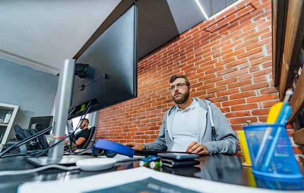 Bearded male computer programmer in glasses develops new technologies at his workplace.