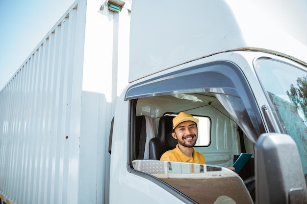 写真 制服を着たひげの男性配達員が貨物トラックを運転する前に笑顔で座っています