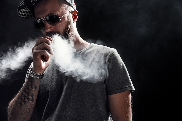 Photo bearded male dressed in a grey shirt, sunglasses and baseball cap vaping