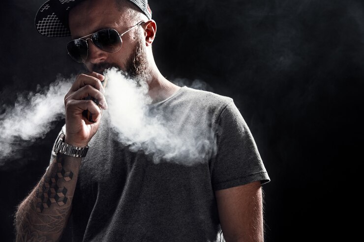 Photo bearded male dressed in a grey shirt, sunglasses and baseball cap vaping