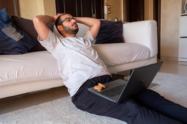 bearded male drinks coffee while working on his laptop from his home and eating cookies